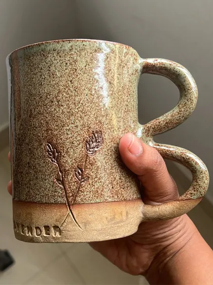 A beautiful hand-built mug from a workshop, featuring a carved lavender sprig and a comfortable, unique handle.