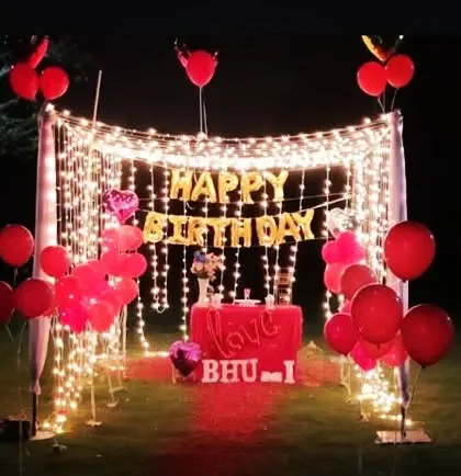For more intimate celebrations, I design romantic outdoor birthday setups like this one. It features a canopy of fairy lights, "Happy Birthday" foil balloons, and simple red balloon decor to create a magical and personal atmosphere.