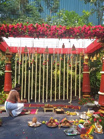 A priest setting up for a ceremony at a traditional red-pillared mandap.