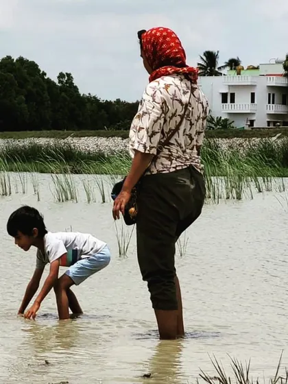 An instructor and child work side-by-side in the water, digging for the best clay deposits.