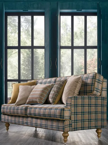 A classic sofa upholstered in a timeless plaid fabric. The shot is framed by large windows, creating a bright and airy feel that showcases the fabric in natural light.
