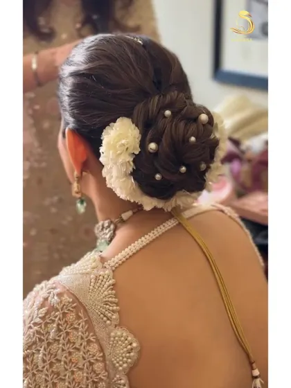 A close-up of a textured bridal bun. The combination of white flowers and scattered pearls creates a look of pure elegance, perfect for a pastel lehenga.