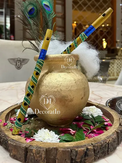 A thematic centerpiece with a golden matki (pot) and decorative flutes, perfect for the Krishna theme.