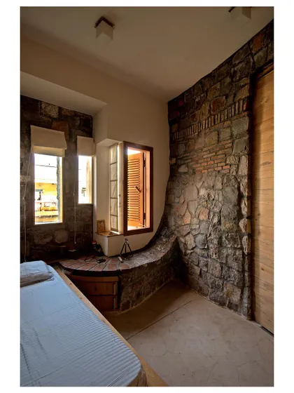 In the bedroom, the stone and brick wall deforms and slopes to create an integrated, rustic seating nook by the window.