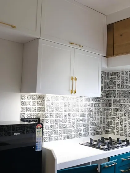 A close-up of the white PU finish upper cabinets with classic gold handles. The design is set against a distinctive black and white patterned tile backsplash, creating a timeless look.