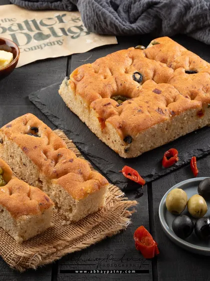 I wanted to show both the whole focaccia bread and a single serving to give customers a complete picture. The ingredients like olives and peppers are scattered around to highlight the flavor.