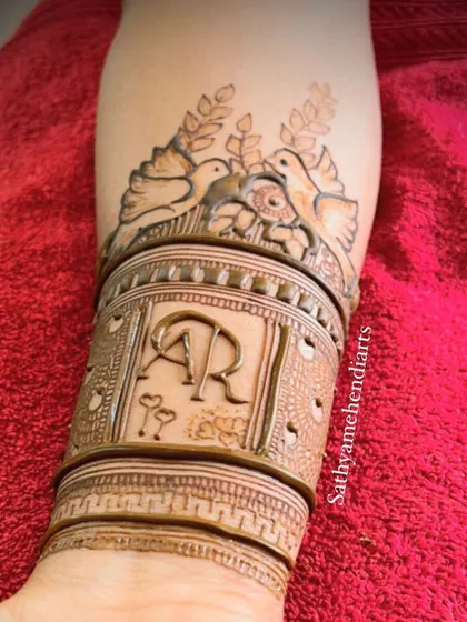 A close up of a custom engagement mehendi cuff. This design features the couple's initials, "AR", along with two lovebirds, symbolizing their new journey together.