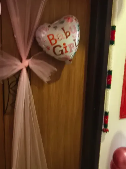 A close-up of the door decor for a baby girl's welcome. A pink tulle bow and a heart-shaped "Baby Girl" balloon make for a sweet and inviting entrance.