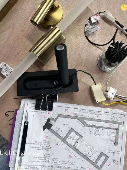 Light fixtures and plans laid out on a workbench at the 58WV site. Selecting the right lighting is a detailed process that involves balancing aesthetics, functionality, and the overall mood of the space.