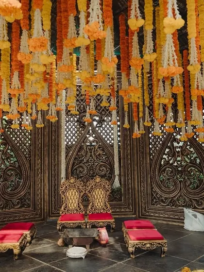 The seating area of the marigold Muhurtham setup, with regal red and gold chairs set against a backdrop of intricate wooden carvings.