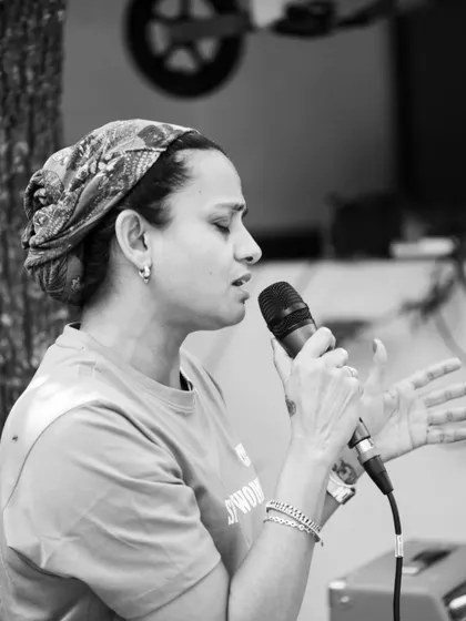 A black and white portrait of one of our members taking the mic at the Garage Sale, sharing her voice with the community.
