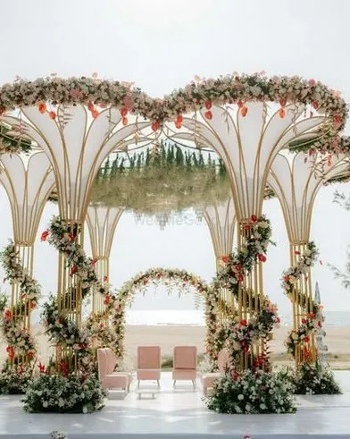 A spectacular destination wedding mandap with unique floral-topped structures spiraling with flowers, set against the ocean.