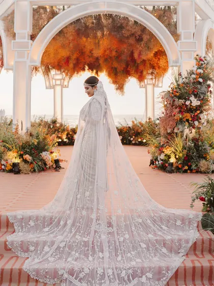 The bride's magnificent train flows down the steps of the sunset-hued mandap. I designed the floral arrangements to complement her elegance and the romantic seaside setting.