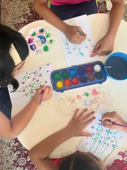An overhead view of a watercolor flower painting session. This activity helps children practice fine motor skills as they paint delicate stems and petals.