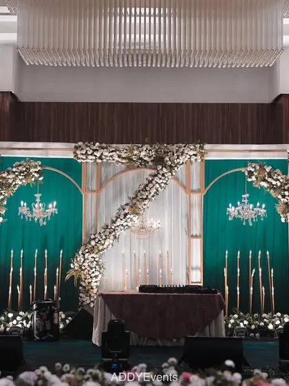 This stage combines emerald green drapery with white floral arrangements and elegant chandeliers. The design is perfect for a formal engagement or a sophisticated corporate event, showcasing a blend of classic and modern aesthetics.