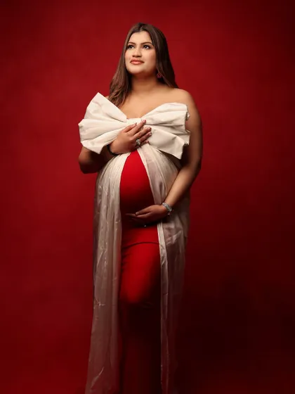 A stunning frontal view of the mother-to-be, wrapped like a precious gift in a red gown and a large white bow. This portrait is a beautiful way to celebrate a pregnancy during the festive season.