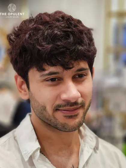 A subtle yet striking men's hair color makeover. This deep burgundy hue adds a touch of personality and edge, perfectly blended into his natural texture for a modern look.