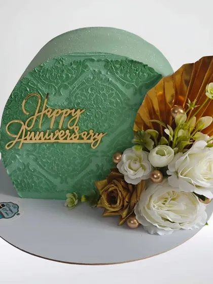 A modern "top forward" anniversary cake with a beautiful sage green stencil pattern. The arrangement of white and gold flowers adds an elegant and artistic flair.