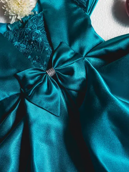 Make a statement in this stunning midnight blue satin gown. The bodice is adorned with intricate sequined lace, and a large bow with a silver ribbon center adds a final touch of sophisticated sparkle.