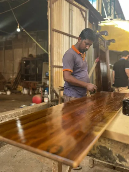 The final polish. One of our skilled craftsmen applies the finishing coat to a tabletop, bringing out the wood's natural grain and shine. This final step is crucial for both durability and beauty.