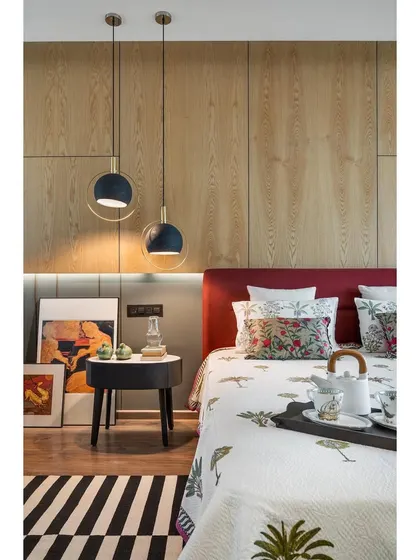 A detail of the master bedroom in apartment 5212, where modern pendant lights hang beside the carmine-red headboard.