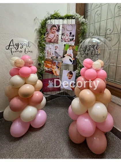 Balloon columns topped with personalized bubble balloons, flanking a photo display grid for a first birthday party.