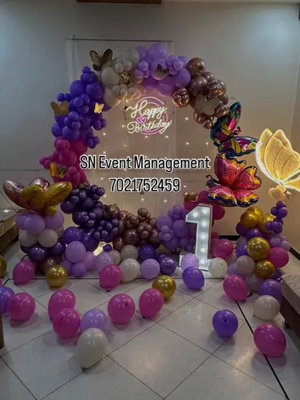 A stunning butterfly-themed balloon ring in shades of purple and gold. The decoration includes light-up butterflies and a marquee number '1', creating a magical centerpiece.