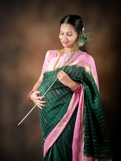 A solo portrait in a traditional green and pink saree, accessorized with a peacock feather. This studio shot has a divine and serene quality.