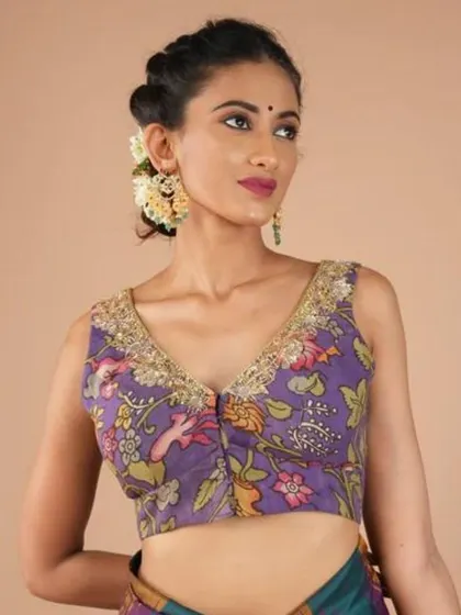 This sleeveless V-neck blouse in a lovely lavender hue features a delicate Kalamkari floral print. The gold embroidery along the neckline adds a touch of festive sparkle.