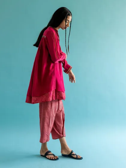 A full-length side profile for Swatti Kapoor. The simple composition against a solid blue wall showcases the silhouette and layering of the contemporary ethnic outfit.