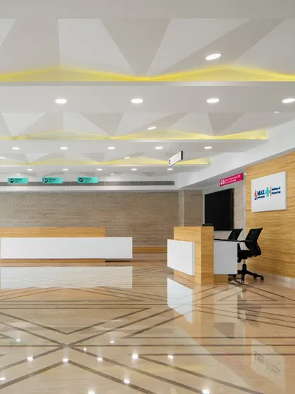 The reception area at Max Patient Services features a geometric ceiling design and a mix of warm wood and clean white surfaces. This combination of materials and forms creates a visually engaging yet orderly environment for arriving patients.