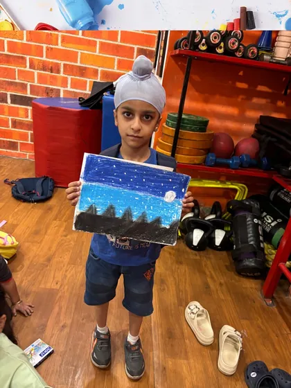 A student proudly presents his night-sky drawing. Our classes help children learn to represent the world around them through art.