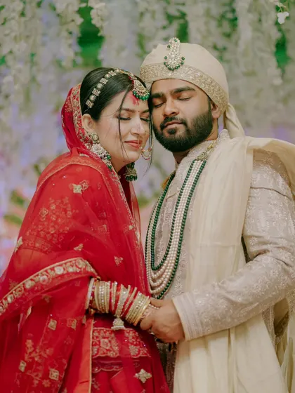 An intimate portrait of a North Indian couple, holding each other close. The rich red of the bride's lehenga and the groom's elegant sherwani create a timeless image of love and commitment.