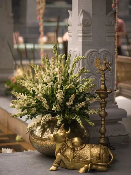 Traditional elements bring a sense of sanctity and grace. A brass Nandi statue and a traditional lamp sit beside a floral arrangement, adding a touch of royal, cultural elegance to the wedding decor.