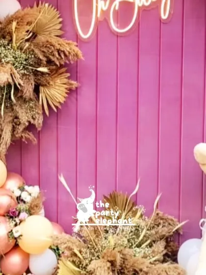 A detail shot of the baby shower backdrop, focusing on the 'Oh Baby' neon sign, the cute teddy bear, and the arrangements of dried pampas grass that added a rustic texture.