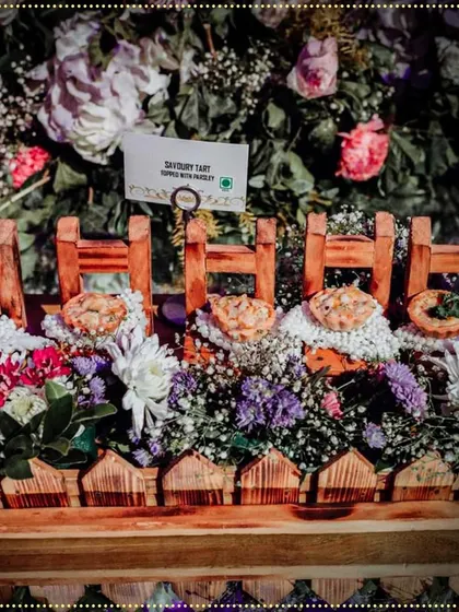 Savory tarts nestled in a bed of flowers within a charming wooden fence-like container, a creative and whimsical food presentation.
