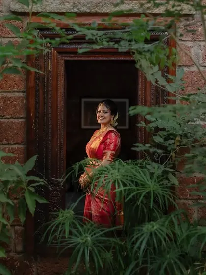 A portrait of the bride in her stunning red saree, framed by the rustic charm of her wedding venue. We focus on creating images that are both beautiful and full of character.