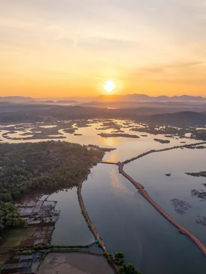 A golden sunrise over the Aghanashini river in Kumta. This high-angle aerial shot captures the light hitting the water and the distant hills, showcasing the beauty of the Uttara Kannada region.