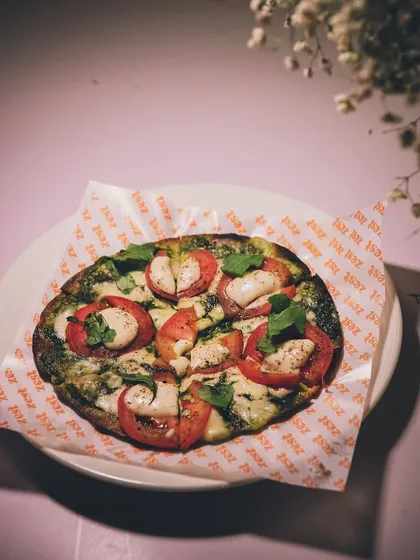 A gourmet pizza with pesto, fresh tomatoes, and mozzarella, served on branded paper.