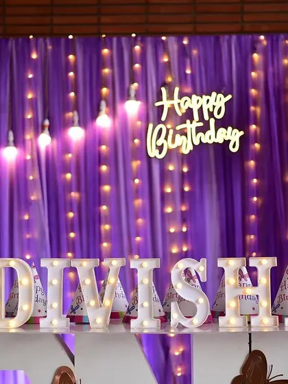 I designed this butterfly-themed backdrop with purple drapes, fairy lights, and a "Happy Birthday" neon sign. The baby's name in marquee letters adds a personalized touch to the cake table area.