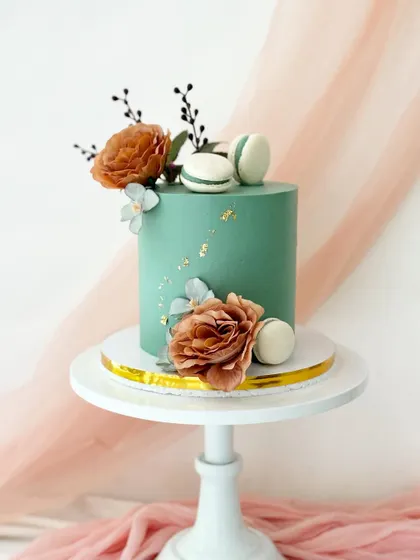 A sophisticated sage green cake with gold leaf flecks. The cake is adorned with rustic orange-toned flowers and light blue macarons for a modern, earthy color combination.
