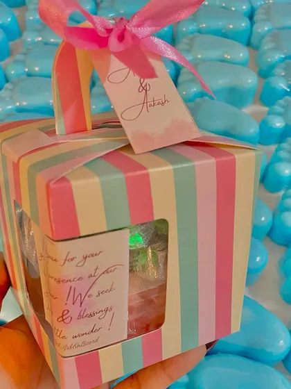 This baby shower favor box includes a candle and foot-shaped soaps, all tied with a pink ribbon and a personalized tag.