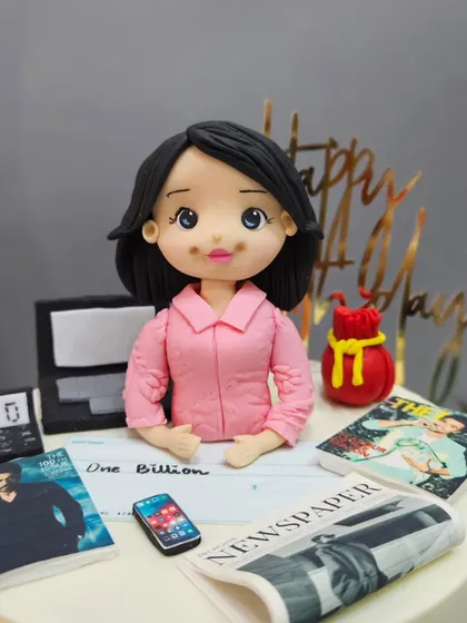 A close-up of the PR expert figurine, sitting at her desk with a miniature laptop, newspaper, and magazines.