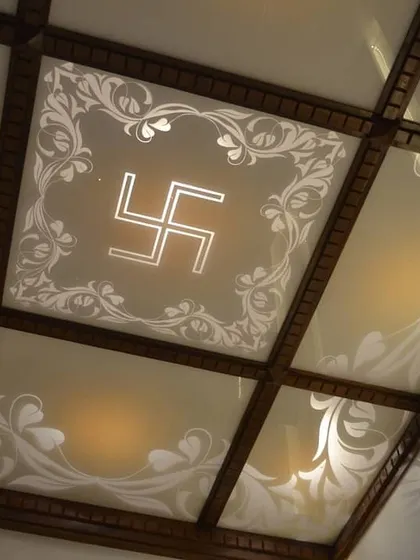 A custom-designed ceiling for a sacred or traditional space, featuring frosted glass panels with etched floral motifs. The central panel is highlighted with an illuminated Swastika symbol, blending spiritual significance with elegant design.