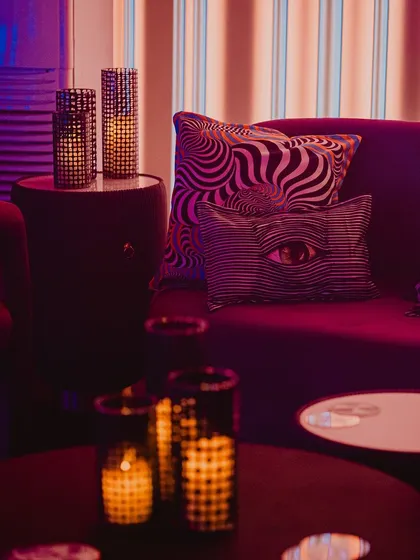A detail shot of the lounge seating, featuring a plush purple sofa and cushions with psychedelic and graphic prints, reinforcing the edgy, modern theme.