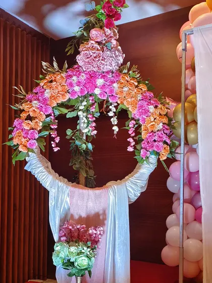 This modern floral hoop is a unique and stylish alternative to a traditional backdrop for a naming ceremony. The ring is decorated with a lush arrangement of pink and orange flowers, creating a vibrant focal point.