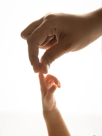 The delicate touch between a parent's hand and their baby's tiny fingers. This backlit, artistic shot highlights the beautiful, fleeting details of the newborn stage.