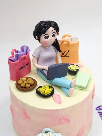 This cake is a perfect tribute to someone who loves shopping and relaxing. The topper includes a personalized figurine with a laptop, snacks, and miniature shopping bags from favorite brands.