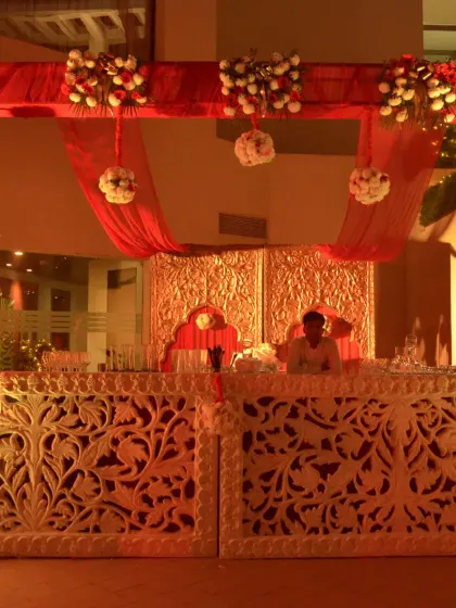 A beautifully carved bar counter with intricate details, illuminated from within. The red and gold draping above adds a touch of traditional luxury.
