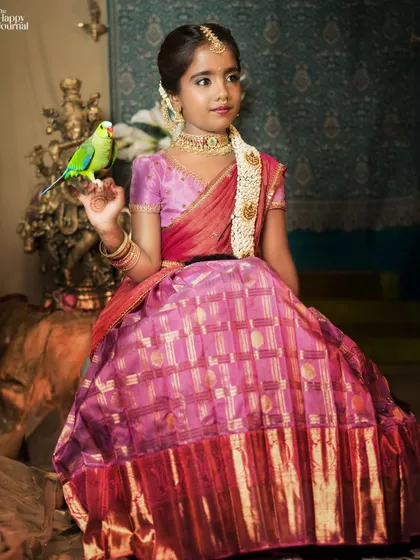 A girl in a traditional silk lehenga sits gracefully with a parrot on her hand, creating a regal and enchanting portrait.